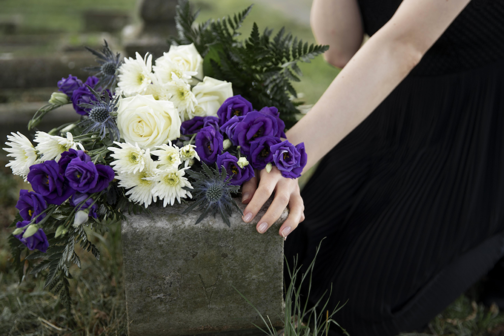 Close up of a woman's hand and a bunch of white and purple flowers on a grave