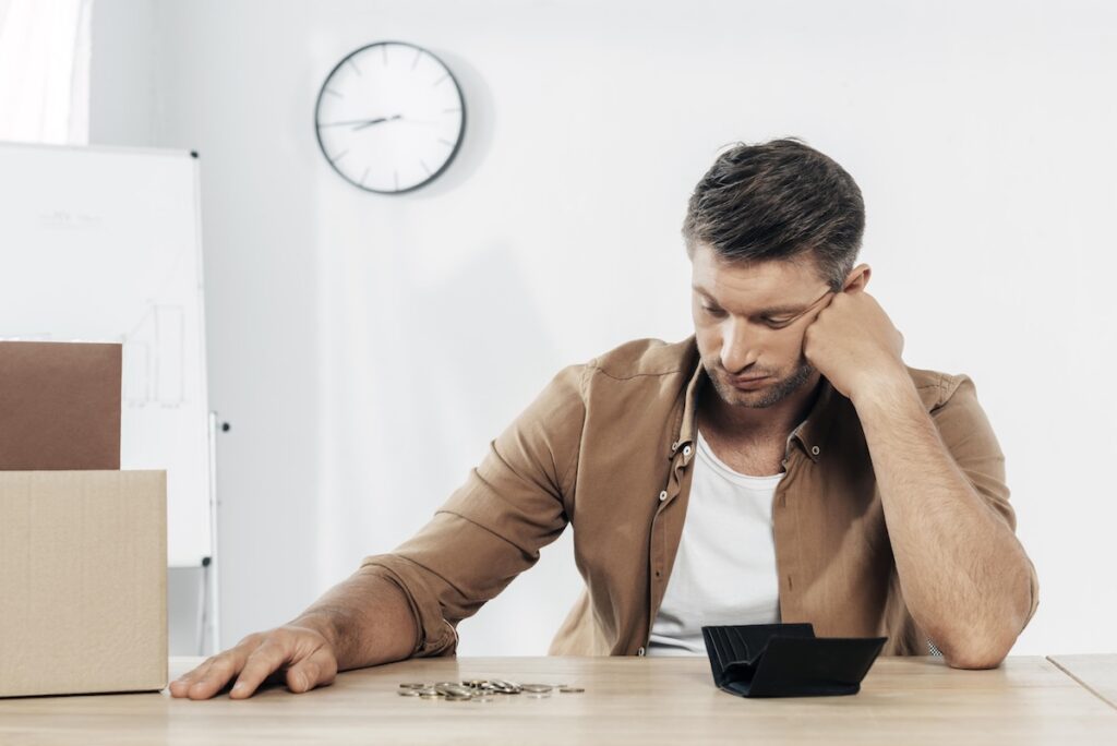 Young man with tired expression looking at a small pile of coins.