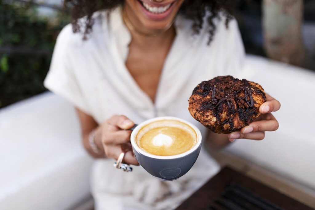 Close up of a woman holding a cup of coffee and a cake
