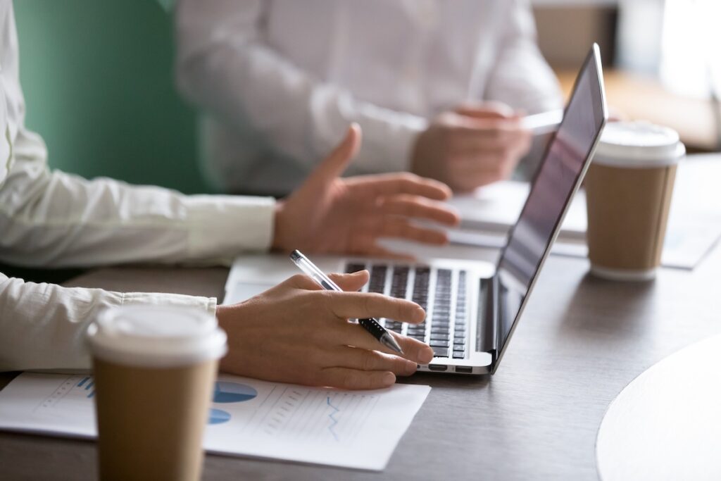 Close up of woman's hands, using laptop and making a presentation using notes with statistics.