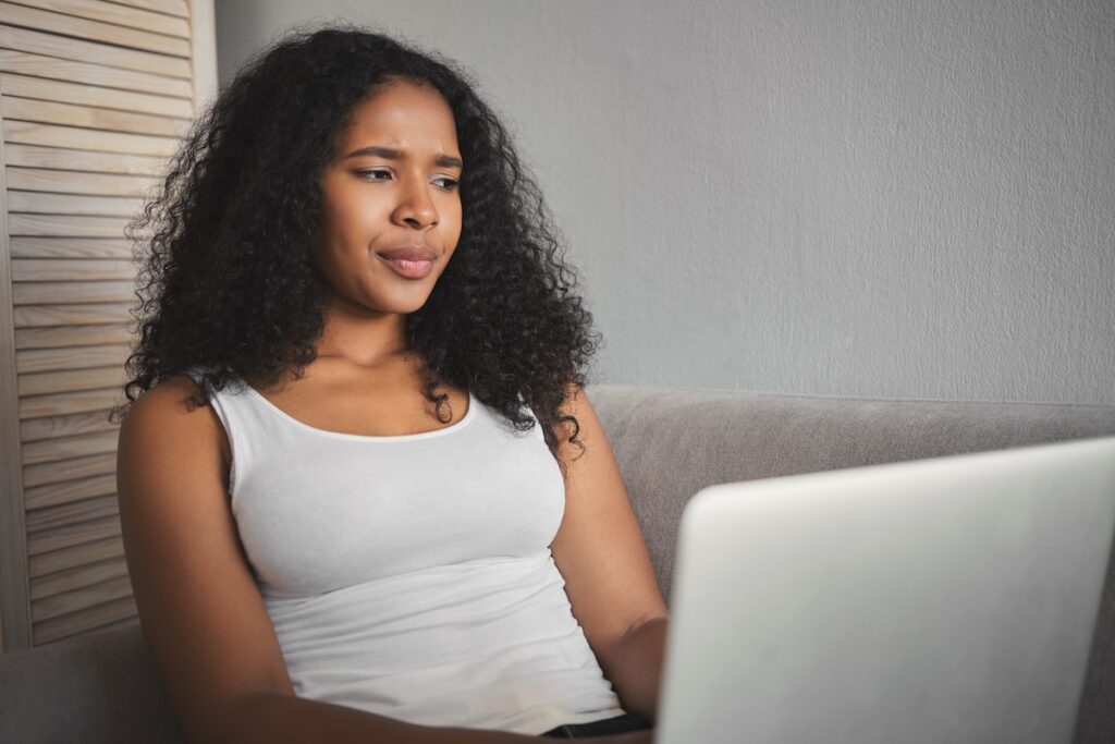 oung black woman sitting in front of a laptop looking confused and frustrated