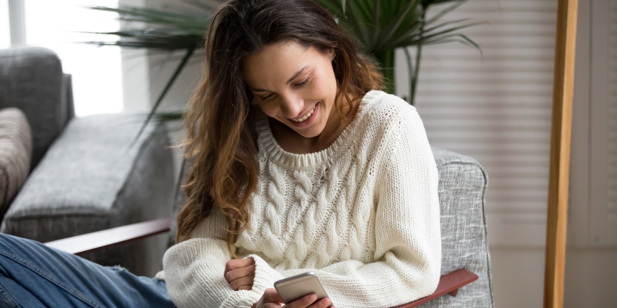 Smiling young woman in an armchair looking at mobile phone