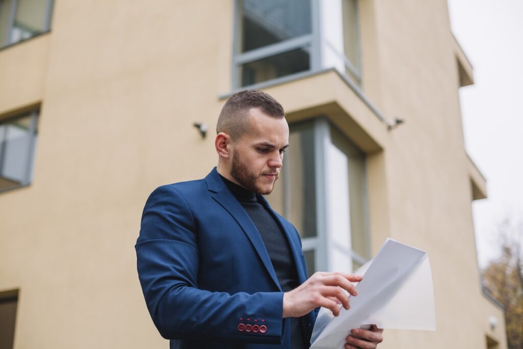 Man looking at papers outside a block of flats.